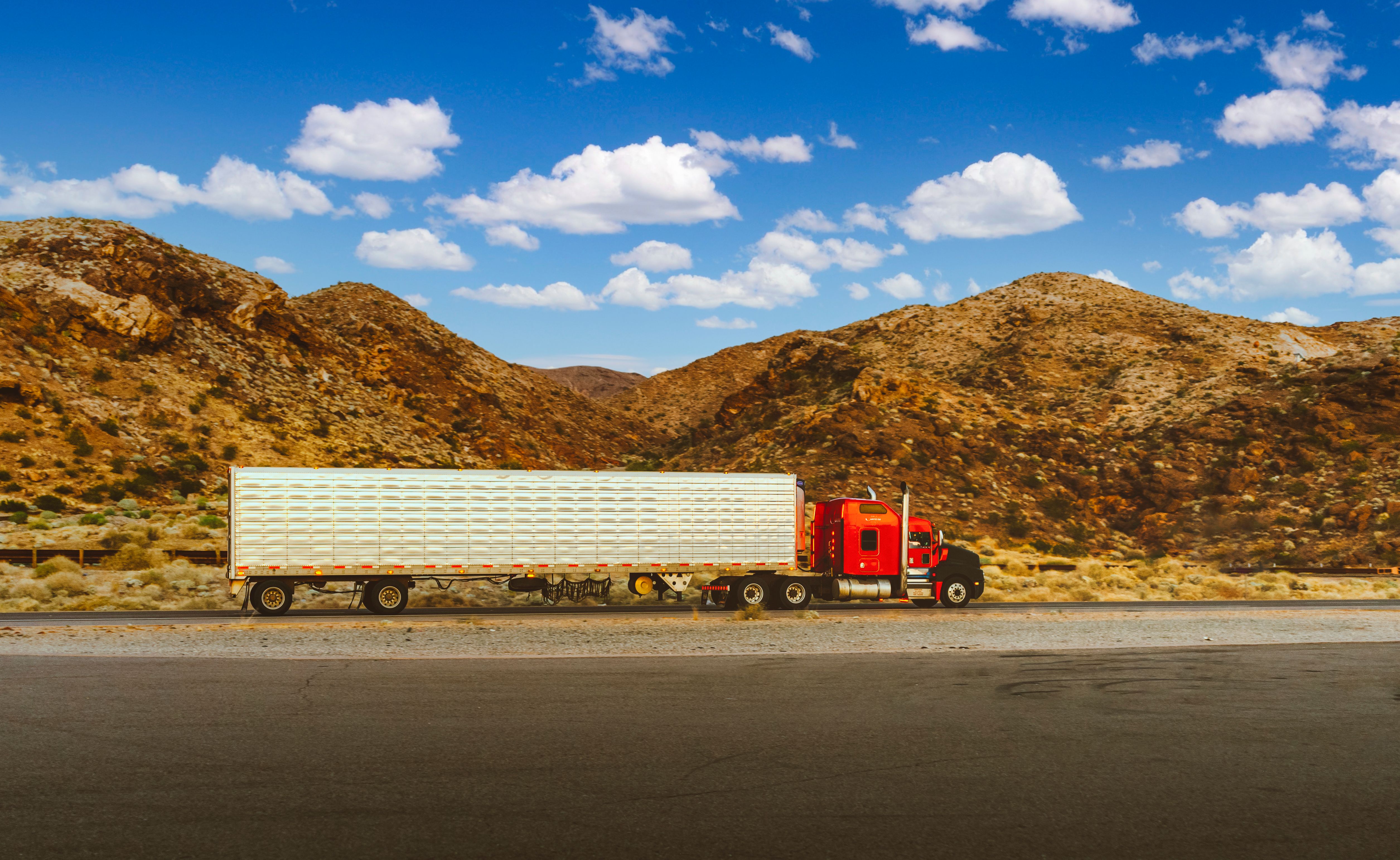 A semi truck traveling a desert highway with mountains in the distance